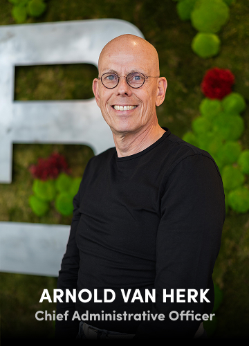 Portrait of Arnold van Herk, Chief Administrative Officer, wearing a black shirt with a green wall background.