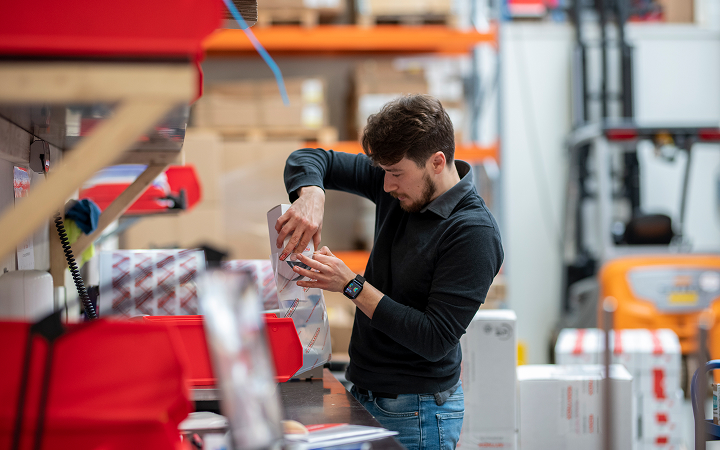 A worker in a warehouse assembling or packaging an item at a workstation.