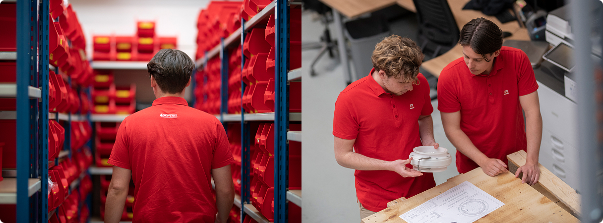 Two team members in red shirts collaborating in a workspace filled with tools and red containers.