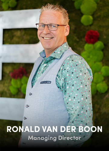 Portrait of Ronald van der Boon, Managing Director, wearing a patterned shirt and vest with a green wall backdrop.