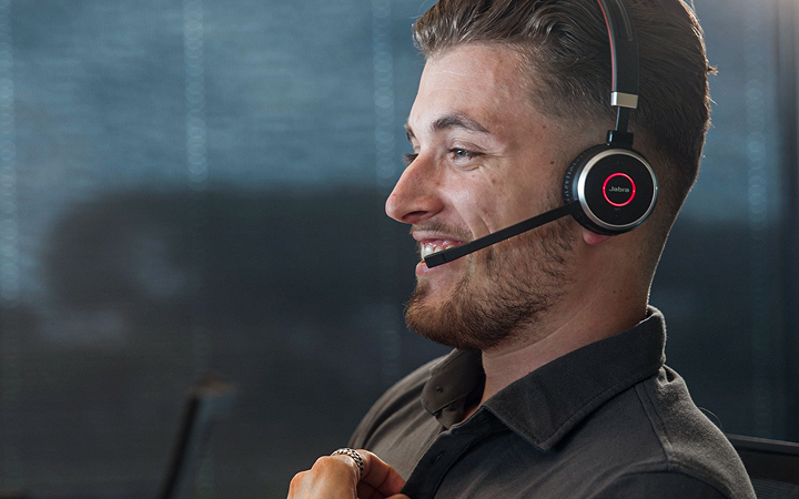 A sales engineer wearing a headset, smiling during a call in an office setting.