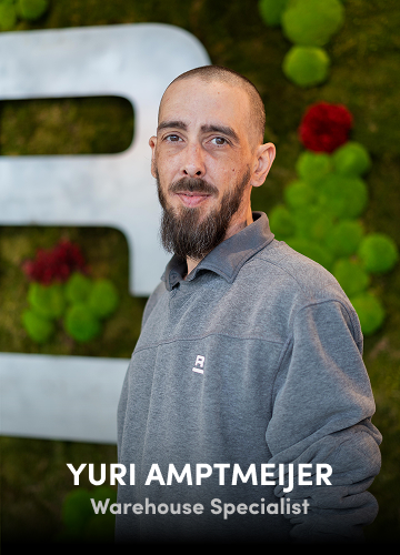 Portrait of Yuri Amptmeijer, Warehouse Specialist, in a grey shirt with a green wall background.