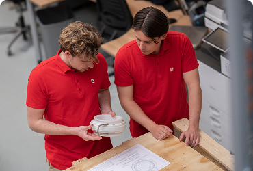 Two employees in red polos examining a part and discussing a technical drawing